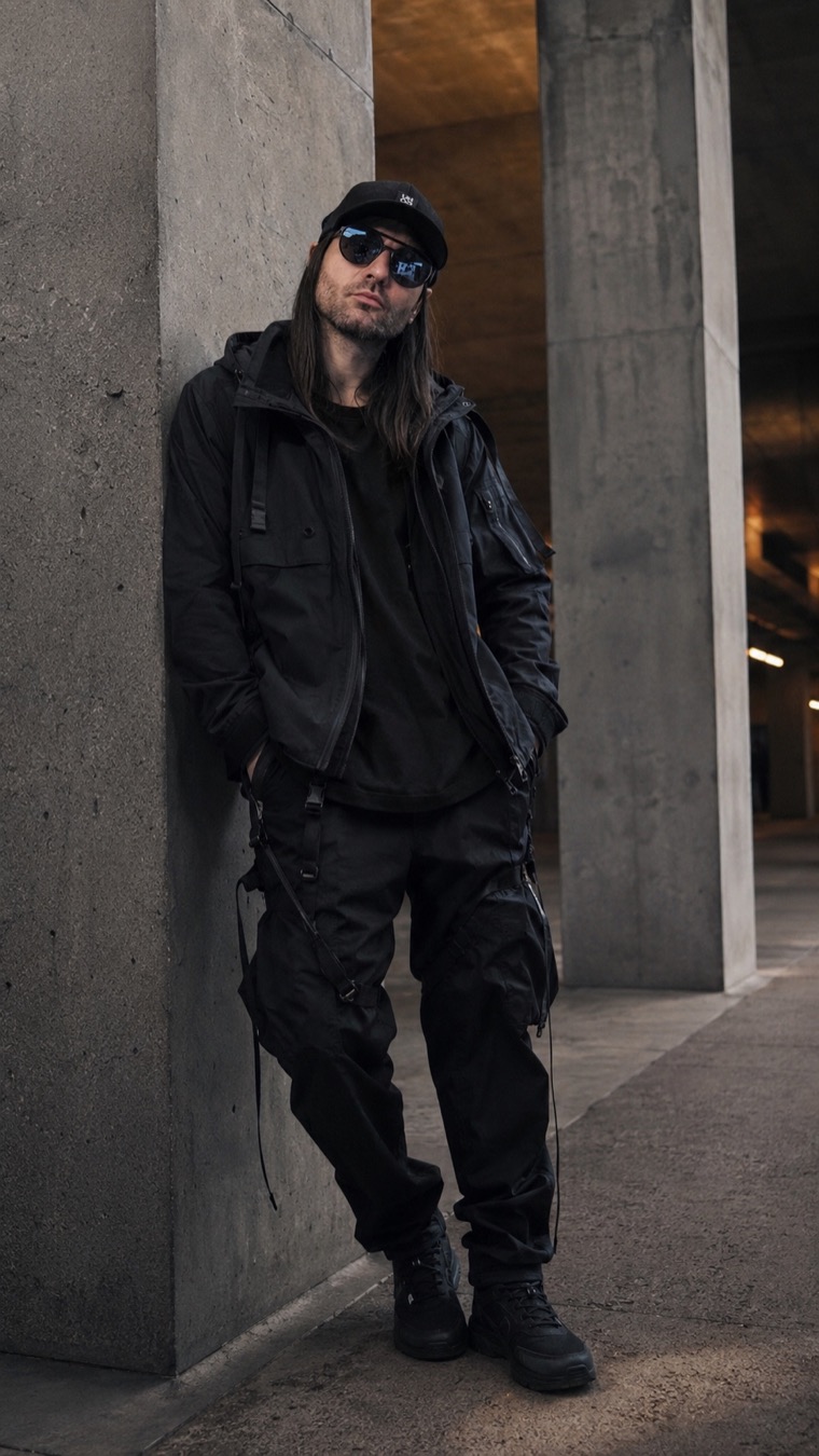 Katze leaning on a concrete column in black technical clothing